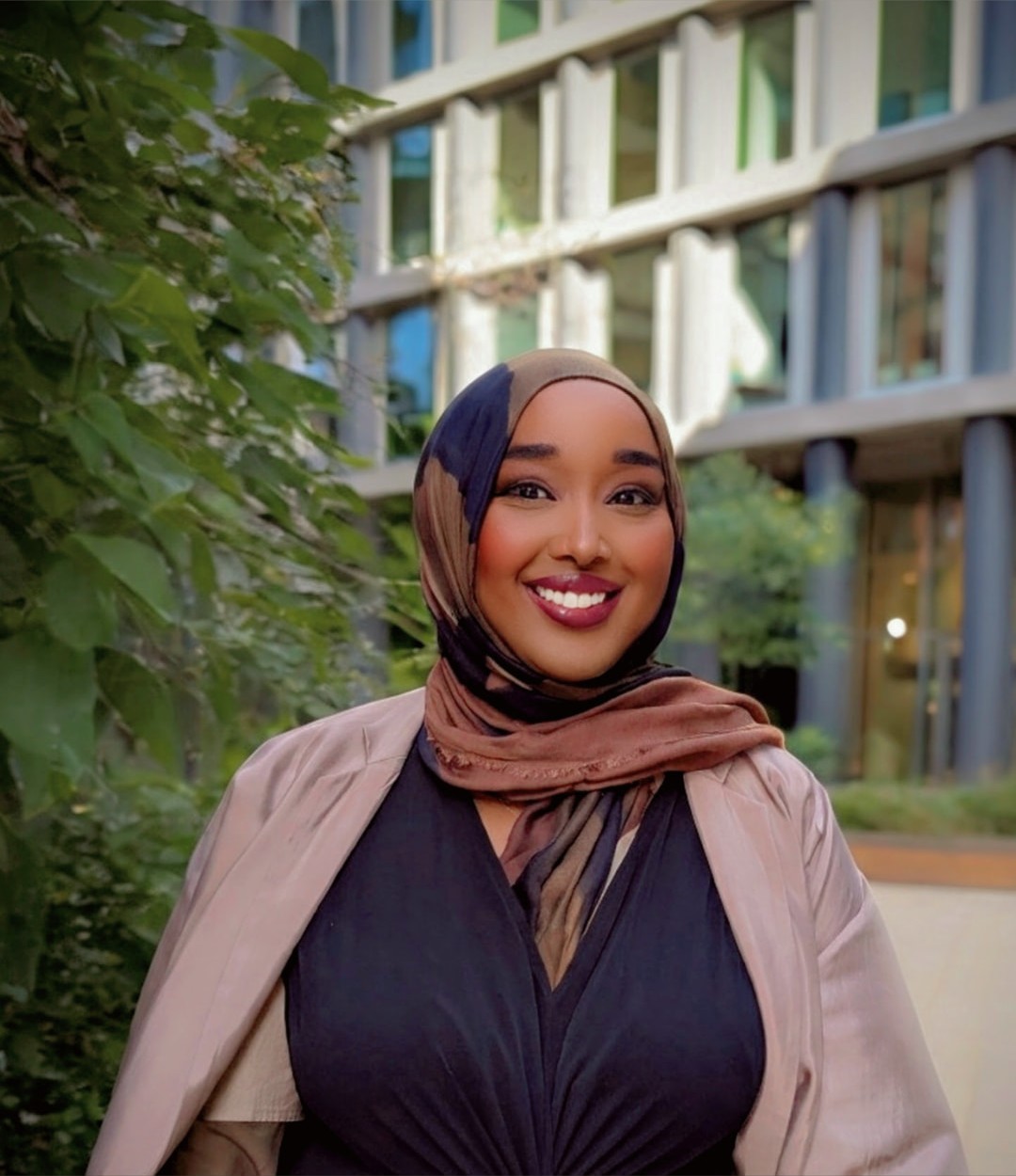 Ayan Obseyeh, CorpWell co-founder, wearing a headscarf and smiling outside a modern office building