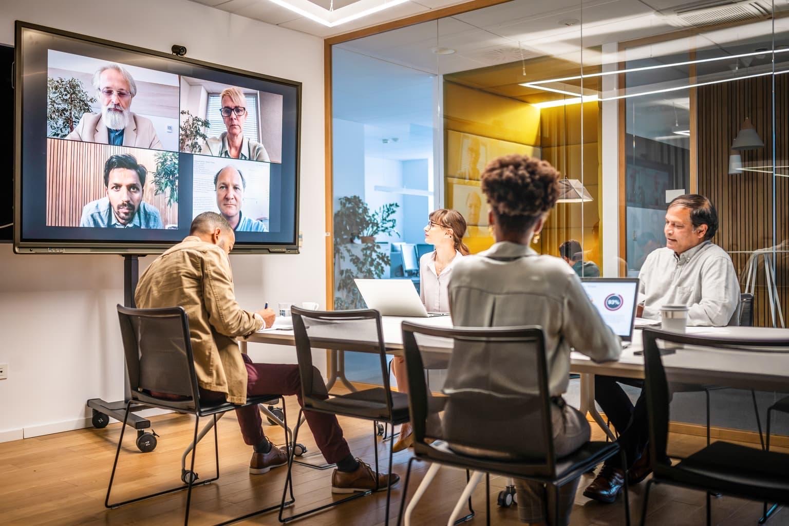 A hybrid team meeting with colleagues in the room and others joining by video
